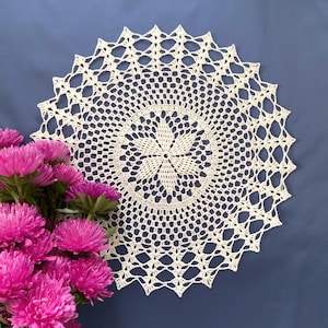 Peut inclure: Une dentelle crochetée blanche avec un motif floral délicat. La dentelle est circulaire et a un bord festonné.