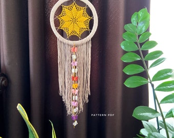Peut inclure: Un attrape-rêves crocheté jaune et blanc avec une frange perlée et des accents de papillons colorés. L'attrape-rêves est suspendu à un rideau marron. Le texte "PATTERN PDF" est visible en bas de l'image.