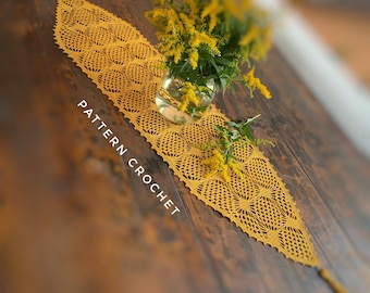 May include: A crocheted table runner in a mustard yellow color with a delicate pattern. The runner is laid on a wooden table with a bouquet of yellow flowers in a glass vase.