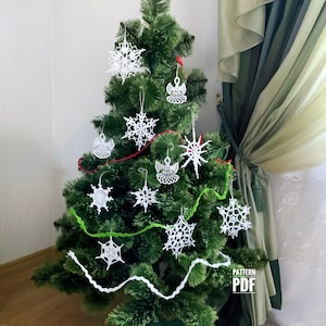 Puede incluir: Un árbol de Navidad decorado con adornos blancos de copos de nieve y ángeles. El árbol está adornado con guirnaldas rojas y verdes. Los adornos están hechos de un material delicado y de encaje. El árbol está colocado contra una pared neutra y una cortina verde.