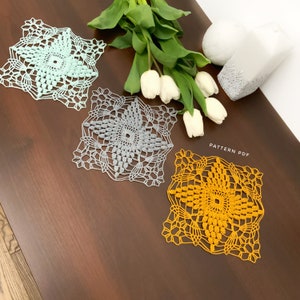 Könnte beinhalten: Drei gehäkelte Deckchen in verschiedenen Farben: hellblau, grau und gelb. Die Deckchen sind quadratisch und haben ein Sternmuster in der Mitte. Die Deckchen liegen auf einer Holzoberfläche. Der Text "PATTERN PDF" ist im Bild sichtbar.
