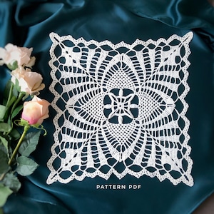 May include: A white crocheted square doily with a delicate floral pattern. The doily is on a teal fabric background. The text "PATTERN PDF" is printed below the doily.
