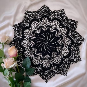 Könnte beinhalten: Schwarze Häkeldeckchen mit einem zarten Blumenmuster. Das Deckchen ist rund und hat ein Sternmuster in der Mitte.