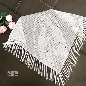 Op de afbeelding: Een witte driehoekige gehaakte sjaal met een gedetailleerd opengewerkt patroon dat de afbeelding vormt van een figuur met een hoofdbedekking. De sjaal heeft lange franjes langs twee randen en bevat de tekst PATTERN PDF in de linkerbenedenhoek.