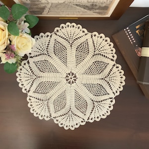Peut inclure: Une nappe en crochet blanche avec un motif floral délicat. La nappe est ronde et a un bord festonné.