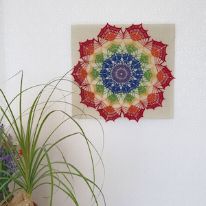May include: A rainbow crochet mandala with a white background. The mandala is made of different colored yarn and has a circular design.