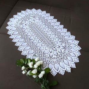 Pu&ograve; includere: Un runner da tavolo ovale in crochet bianco con un delicato motivo floreale. Il runner &egrave; realizzato con un filo sottile e ha un bordo smerlato.
