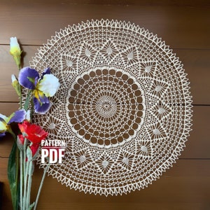May include: A cream-colored, circular crochet doily with a detailed floral pattern. The doily is displayed against a brown wooden background, with a vase of colorful flowers to the left. The text "PATTERN PDF" is visible.