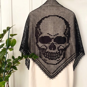 Peut inclure: Châle en crochet noir avec un motif de crâne. Le châle est fabriqué dans un tissu en forme de filet, avec un motif de crâne proéminent au centre. Les bords sont finis avec une bordure décorative, ce qui en fait un accessoire distinctif.