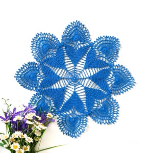 May include: A blue crocheted doily with a delicate floral pattern. The doily is circular and has a diameter of approximately 12 inches.