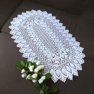 Pu&ograve; includere: Un runner da tavolo ovale in crochet bianco con un motivo delicato e intricato. Il runner &egrave; realizzato con un filo sottile e ha un bordo smerlato.
