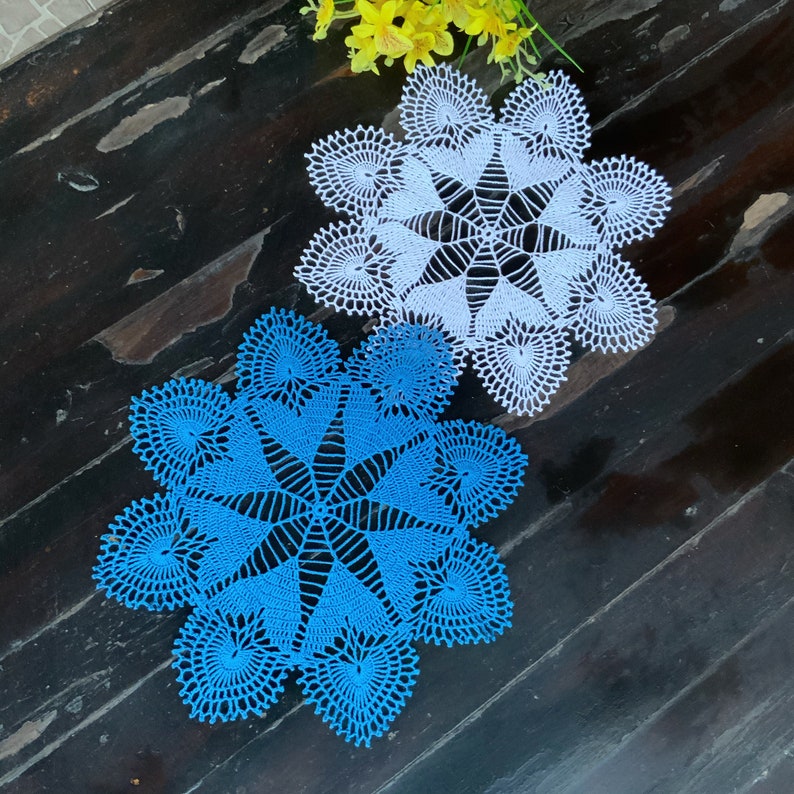 May include: Two crocheted doilies, one blue and one white, with a starburst pattern. The doilies are on a dark wood surface.