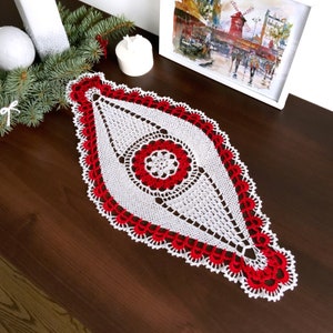 Peut inclure: Un chemin de table en crochet blanc avec un motif central en crochet rouge. Le chemin de table est sur une surface en bois foncé.