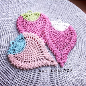 May include: Three crocheted heart-shaped doilies in pink, white, and blue with a green center. The doilies are on a gray textured surface. PATTERN PDF.