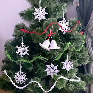 May include: A green artificial Christmas tree decorated with white crocheted snowflakes and bells. The tree is adorned with red and green garland.