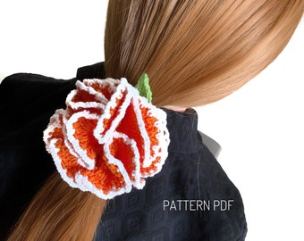 May include: A crocheted orange and white flower hair tie with a green stem. The hair tie is worn in a woman's long, red hair. The text "PATTERN PDF" is visible on the image.