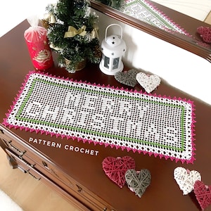 May include: White crochet table runner with a green and pink border. The runner has a delicate floral pattern and the text "PATTERN CROCHET" is written on the table surface.