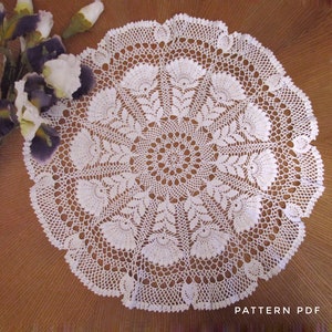May include: A white, circular, crocheted doily with a detailed floral pattern. The doily is placed on a brown wooden surface. The text "PATTERN PDF" is visible in the lower right corner. The doily is a handmade craft item.