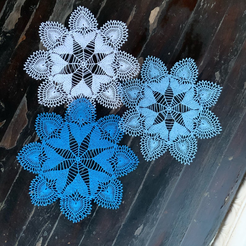 May include: Three crocheted doilies in shades of blue and white. The doilies are circular and have a delicate, lacy design.