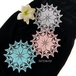 May include: Three crocheted doilies in different colors: light blue, pink, and white. The doilies are laid out on a black fabric background. The text "PATTERN PDF" is visible in the bottom center of the image.