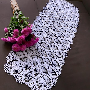 Peut inclure: Un chemin de table en crochet blanc avec un motif délicat et complexe. Le chemin de table est fait de fil fin et a un bord festonné.