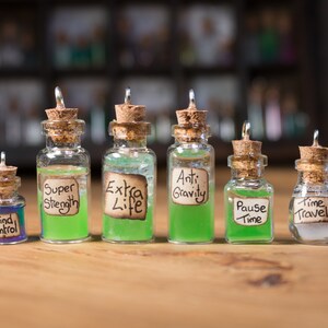 Puede incluir: Siete pequeñas botellas de vidrio con tapones de corcho y etiquetas. Las botellas contienen líquido verde y azul. Las etiquetas dicen "Control mental", "Super fuerza", "Vida extra", "Anti gravedad", "Pausar tiempo" y "Viaje en el tiempo".