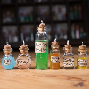 May include: Seven small glass bottles with cork stoppers and labels. The bottles contain different coloured liquids and have labels that read "Zombie Cure", "Brains", "Zombie Antidote", "Zombie Virus", "Zombie Blood", and "Zombie Vaccine".