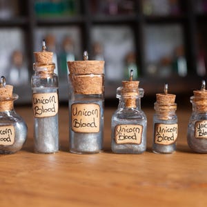 May include: Six small glass bottles with cork stoppers and silver glitter inside. Each bottle has a label that reads "Unicorn Blood".
