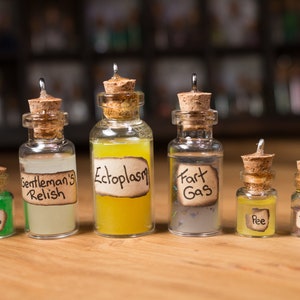 May include: Seven small glass bottles with cork stoppers and labels. The labels have handwritten text, including "Goo", "Gentleman's Relish", "Ectoplasm", "Fart Gas", "Pee", and "Poop".