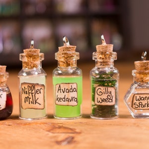 May include: Five small glass potion bottles with cork stoppers. Each bottle contains a different coloured liquid or substance and a label with text: "Elixir of Life", "Nippler Milk", "Avada kedavra", "Gilly Weed", and "Wand Sparks".