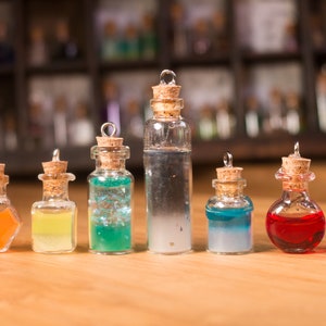 May include: Eight small glass bottles with cork stoppers and silver caps, filled with colourful liquids. The bottles are arranged in a row on a wooden surface.