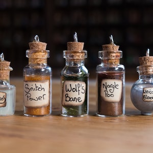May include: Six small glass bottles with cork stoppers and labels. The labels have handwritten text that reads "Lumos", "Snitch Power", "Wolf's Bane", "Nargles Poo", and "Unicorn Blood".