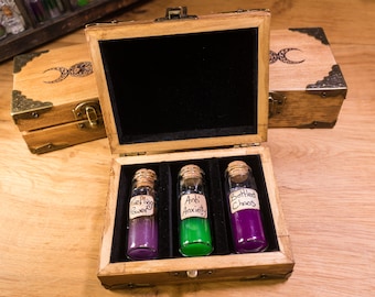 May include: A wooden box with a hinged lid, containing three small glass bottles with cork stoppers. The bottles are filled with purple, green, and purple liquids. The labels on the bottles read "Fieling Power", "Anti Anxiety", and "Bottled Chaos".