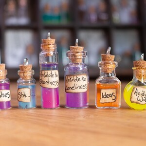 Puede incluir: Seis pequeñas botellas de vidrio con tapones de corcho y etiquetas escritas a mano. Las etiquetas dicen "Wishes", "Shh...", "Antidote to Shortness", "Antidote to Loneliness", "Ideas" y "Acidic Wit".