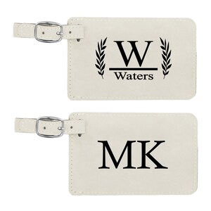 May include: Two white leather luggage tags with black lettering. The first tag has a large "W" with "Waters" underneath and a laurel wreath on each side. The second tag has "MK" in large letters.