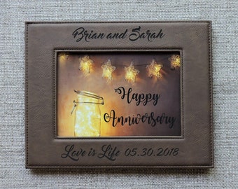 May include: A brown leather picture frame with a photo of a mason jar with lights inside. The frame is engraved with the text "Brian and Sarah", "Happy Anniversary", and "Love is Life 05.30.2018".