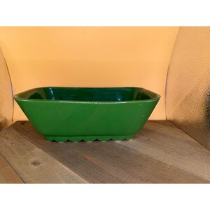 May include: A rectangular green ceramic bowl with a smooth, glossy finish. The bowl features a distinct scalloped base design with rounded edges and a wide, open top, presenting a solid, uniform color throughout the entire exterior surface.