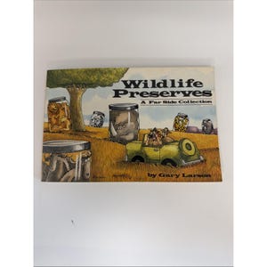 Op de afbeelding: Een paperback boek getiteld Wildlife Preserves: A Far Side Collection door Gary Larson. De kaft bevat een cartoonillustratie van een safarivoertuig en diverse wilde dieren die gevangen zitten in glazen potten in een grasveld.