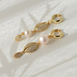 May include: Gold hoop earrings with a pearl and a shell-shaped charm encrusted with clear rhinestones.