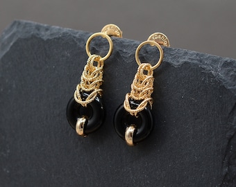 Puede incluir: Un par de pendientes dorados con una cuenta circular negra y un diseño de cadena dorada tejida. Los pendientes tienen un cierre de poste y un pequeño anillo dorado en la parte superior. La palabra "fashion" está estampada en la parte posterior.