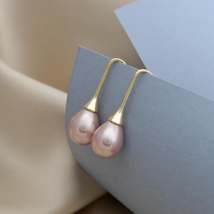 Może przedstawiać: Para złotych kolczyków wiszących z różowymi, perłowymi kamieniami w kształcie łzy.