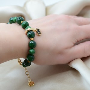 May include: A green jade stone bracelet with a gold charm. The bracelet is made of round beads and has a gold clasp.