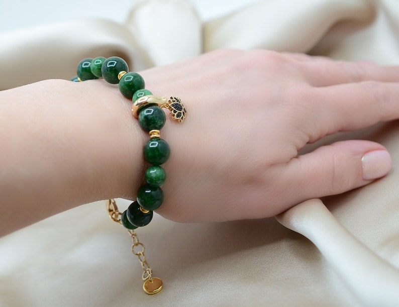May include: A green jade stone bracelet with a gold charm. The bracelet is made of round beads and has a gold clasp.