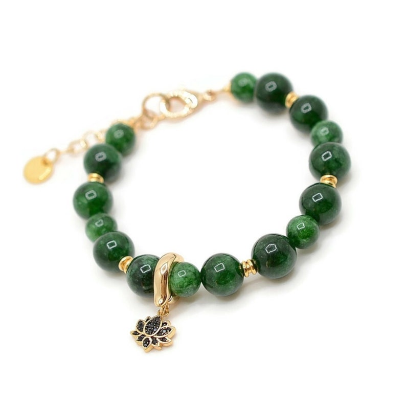 May include: A green jade stone bracelet with a gold clasp and a gold lotus charm. The bracelet is made of round beads and has a simple design.