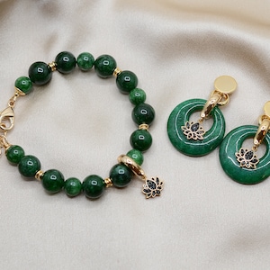 May include: A green jade stone bracelet with a gold clasp and a lotus flower charm. Matching green jade stone earrings with gold hoops and lotus flower charms.