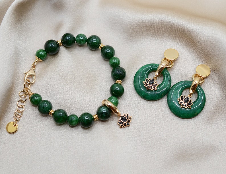 May include: A green jade stone bracelet with a gold clasp and a lotus flower charm. Matching green jade stone earrings with gold hoops and lotus flower charms.