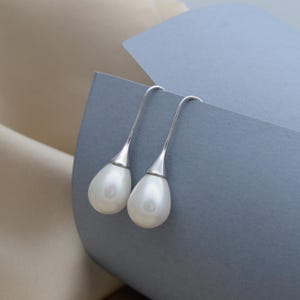 Può includere: Un paio di orecchini pendenti in argento con ciondoli a forma di lacrima di perla bianca.