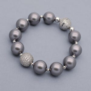 May include: A stretch bracelet featuring large, round, dark gray pearls alternating with two spherical beads encrusted with small, clear, sparkling crystals. The design includes small, polished silver-toned metal spacers between each of the beads.