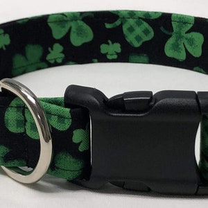 May include: A black dog collar with a green shamrock pattern. The collar has a silver D-ring and a black plastic buckle.