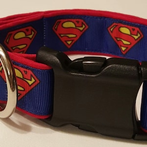 May include: A blue and red dog collar with a repeating pattern of Superman logos. The collar has a black plastic buckle and a silver metal D-ring.